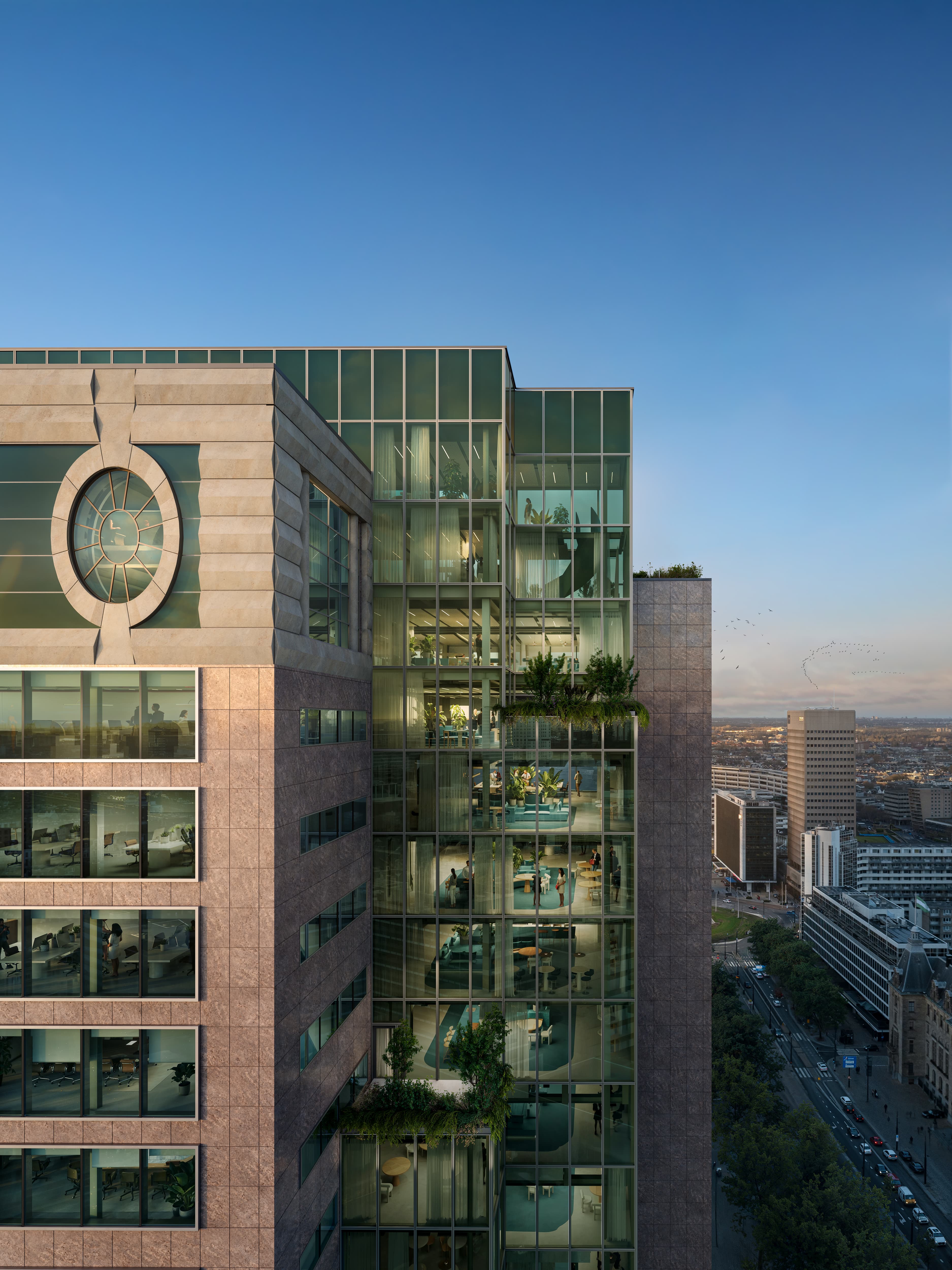 Close-up view of a modern high-rise building featuring a prominent circular window on the left facade and a vertical glass atrium filled with greenery and office spaces on the right. The image is taken at golden hour, with a clear blue sky and distant urban landscape visible in the background.